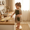 Kinderschortje wafel donkergroen kersenprint rok voorkant, peuter kleuter 2-5 jaar. Meisje van 5 jaar oud is koekjes aan het bakken met een kersen schortje aan van Leonietje's 