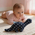 Dinosaurus knuffel Anker donker blauw met labeltjes en rammelaar geluidje. Gemaakt door Leonietje's. op de afbeelding kijkt een baby naar de knuffel tijdens tummy time
